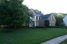 a large brick house sitting on top of a lush green field next to a tree