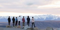 four people standing on top of a mountain looking out at the snow covered mountains in the distance