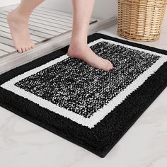 a person standing on a black and white bathroom rug with their feet in the floor