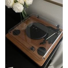 an old record player is sitting on a table with flowers in the vase behind it