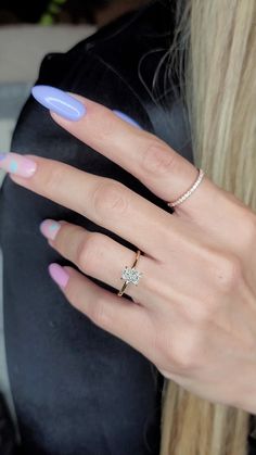 a woman's hand with pink and blue manicured nails holding a diamond ring