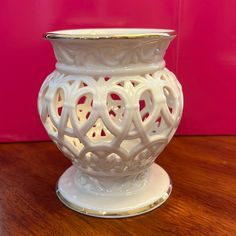 a white vase sitting on top of a wooden table next to a pink wall in the background