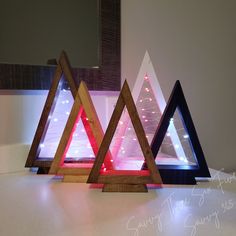 three wooden triangles with lights in them on a counter top next to a mirror that says merry christmas