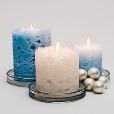 three candles with white and blue frosting next to each other on a plate, surrounded by pearls