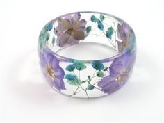 This handmade bangle bracelet features pressed lavender/purple Larkspur & Baby's Breath that are encased in transparent crystal clear resin and shaped into a unique and stylish bangle with a glassy finish that sparkles in the light. It is a chunky bangle with a curved profile; thicker in the center and tapering on the sides. This bangle embodies contemporary resin jewelry for the nature lover. The eco resin is crystal clear plant base resin, UV resistant, strong and environmentally safe. Each pi Handmade Clear Bracelets As Gifts, Handmade Clear Bracelets For Gifts, Handmade Clear Bracelets As A Gift, Clear Bracelet Jewelry Gift, Adjustable Resin Bangle, Lavender Flower Jewelry With Pressed Flowers, Resin Bracelet Jewelry As Gift, Resin Bracelet Jewelry For Gifts, Resin Bracelet Jewelry For Gift