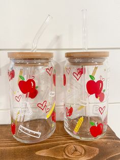 two glass jars with apple designs and strawberries on them sitting on a wooden table