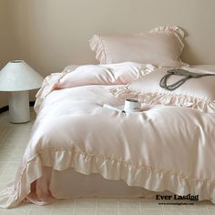 a bed with pink comforter and pillows on it next to a white table lamp