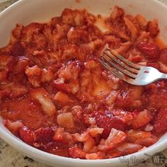 a white bowl filled with pasta and meat on top of a marble counter next to a fork