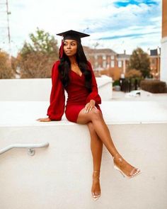 a woman sitting on top of a white wall wearing a graduation cap and red dress