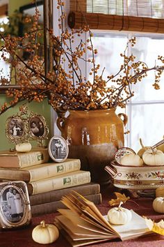 a table topped with lots of books next to a vase filled with flowers and pumpkins