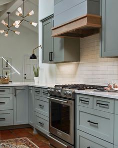 a kitchen with gray cabinets and white counter tops, an oven and stove hood in the center