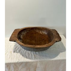 an old wooden bowl sitting on top of a white tablecloth covered table next to a wall