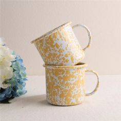 two yellow and white mugs sitting next to each other on a table with flowers