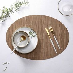 a place setting with silverware and gold utensils on a bamboo table mat