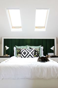 a cat laying on top of a white bed in a room with two skylights