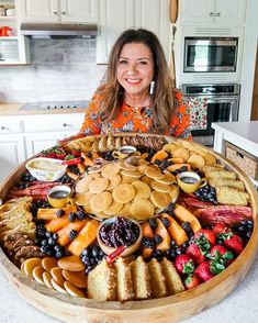 a woman sitting in front of a large platter full of fruit and pastries