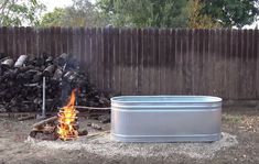 a metal tub sitting in the middle of a yard next to a pile of logs