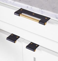 two black handles on a white cabinet with marble counter top in the background and gold hardware