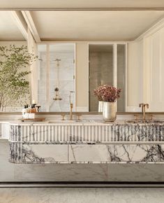 a bathroom with marble counter tops and gold faucets on the sink, along with two vases filled with flowers