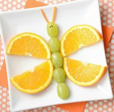 an orange butterfly made out of fruit on a plate next to a glass of juice