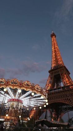 the eiffel tower is lit up at night in front of an amusement park