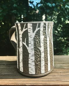 a coffee cup sitting on top of a wooden table in front of some green trees