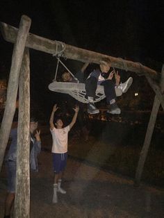 two boys are hanging upside down on a wooden structure while another boy is holding onto the rope