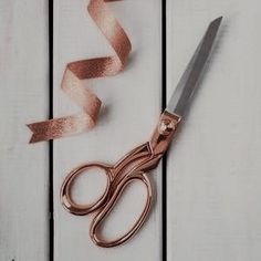 a pair of scissors sitting on top of a white table next to a brown ribbon