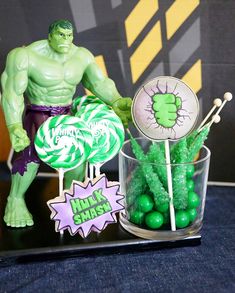 there is a hulk cake topper next to some lollipops in a cup