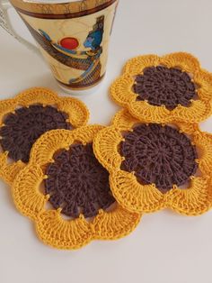 four crocheted coasters sitting next to a coffee cup