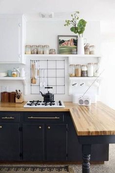 a kitchen with black cabinets and wooden counter tops, white walls and open shelving above the stove