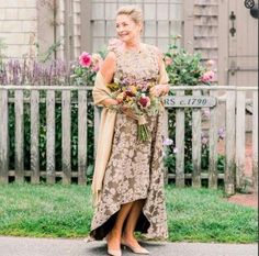 a woman standing in front of a wooden fence holding a bouquet of flowers and smiling at the camera