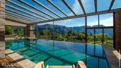 an indoor swimming pool surrounded by wooden decking and glass walls with mountains in the background