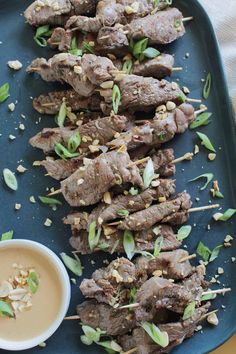 skewers of meat and vegetables on a blue platter with a small bowl of dipping sauce