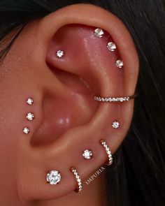 a woman with three different piercings on her ear and behind the ear is a diamond ring