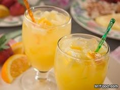 two glasses filled with orange juice sitting on top of a table next to plates of fruit