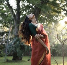 a woman in a red and green sari is holding her head up to the sky