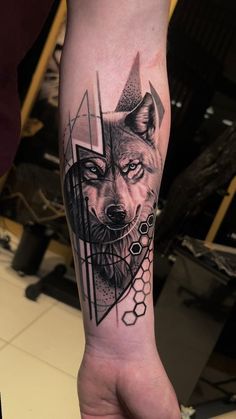 a man's arm with a wolf tattoo and geometric shapes on it, while he is holding his hand in the other hand