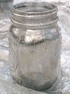 an old silver mason jar sitting on top of a white cloth covered table with other items in the background