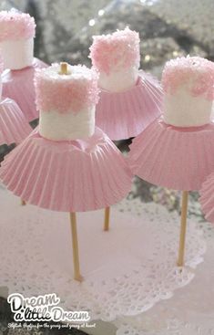 pink and white cupcakes are sitting on top of small sticks with marshmallow tops