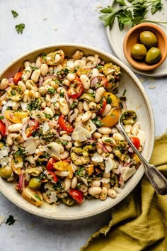 a bowl filled with beans and vegetables on top of a table next to olives