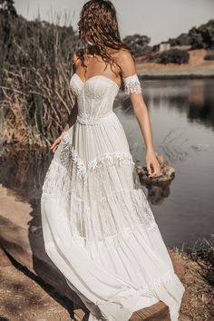 a woman in a white dress is walking by the water with her back to the camera