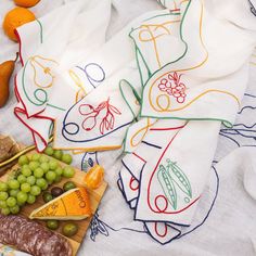 a bunch of food that is laying on a table cloth with some fruit and cheese