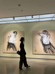 a woman walking past two paintings on display