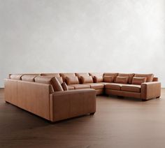 a brown leather sectional sofa sitting on top of a wooden floor next to a white wall