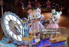 two hello kitty dolls standing on top of a table next to a giant clock and other decorations