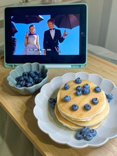 pancakes and blueberries are on a plate in front of a computer screen with the image of a man holding an umbrella