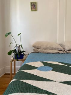 a bed with a blue and green blanket on top of it next to a potted plant