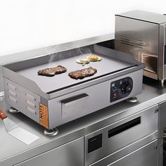 two steaks cooking on top of a grill in a kitchen with stainless steel counter tops