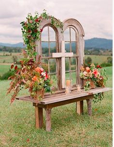 an old window is decorated with flowers and greenery on a bench in the middle of a field